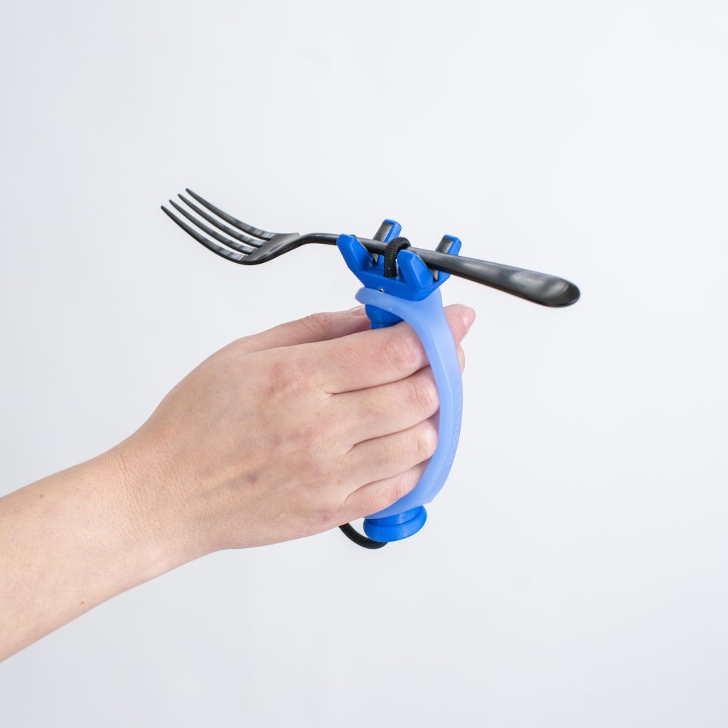 A hand holds a fork with the handle of a FunctionalHand, and a blue EazyHold secures their grip.