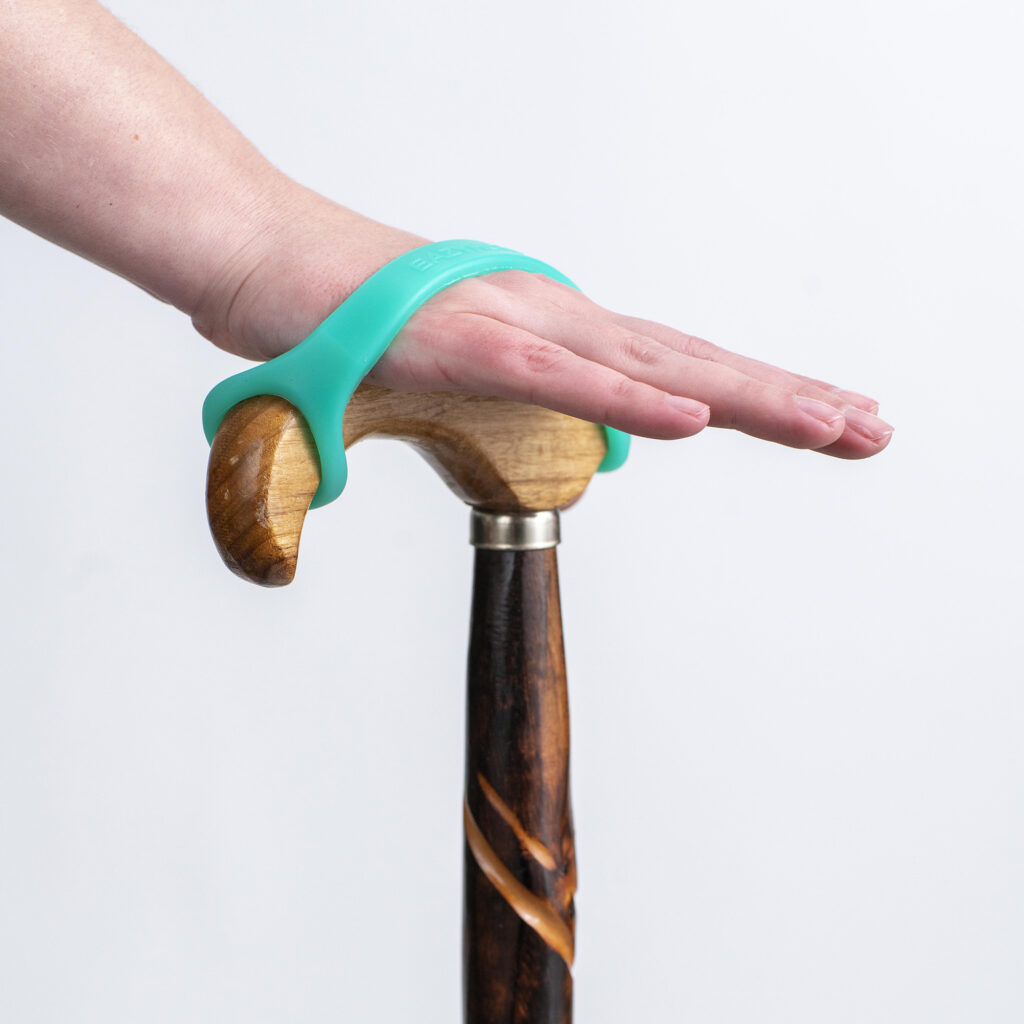 An aqua silicone EasyHold cuff on the handle of a derby handle cane. A flat open hand holds the handle with the help of the cuff