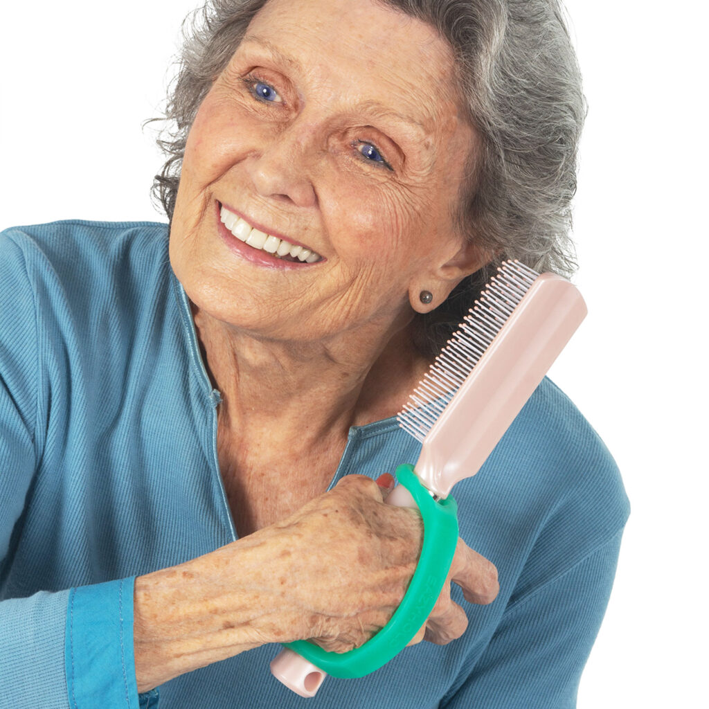 An elderly woman holds a hairbrush with an aqua EasyHold universal cuff on it and over the back of her hand.