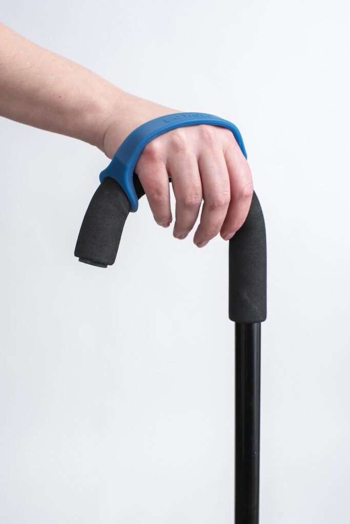 A hand holds a regular black cane with a navy silicone EasyHold cuff on it and over the back of the hand.