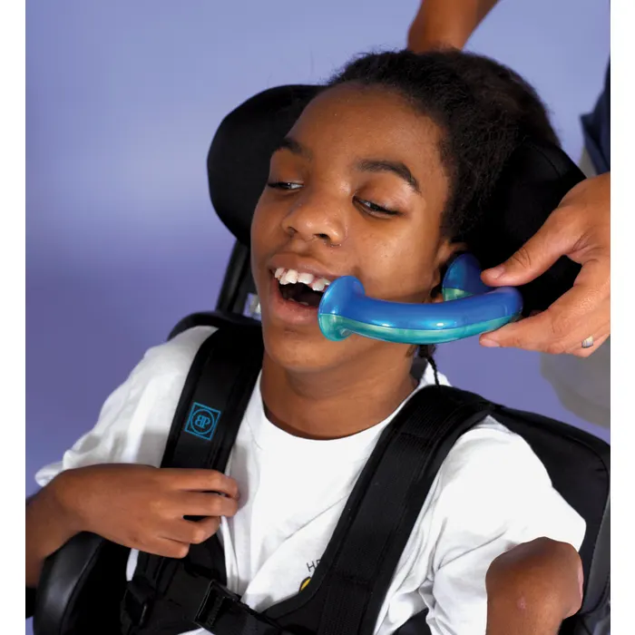 A young child sits in a supportive chair while a teacher or therapist's hand holds the toobaloo listening device up to their ear and mouth, similar to a telephone.