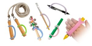 Tools and toys for school that are each equipped with EaZyHold universal cuffs over a white background, including a jump rope, bells, a paintbrush, a marker, a crayon on a small child's hand, and a pen.